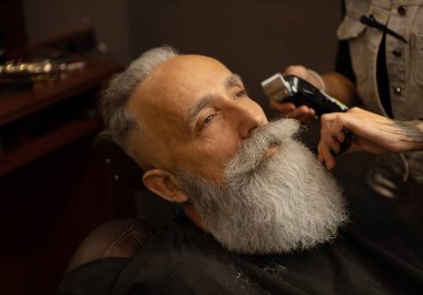 Berber dükkanında kıdemli bir adamın saçlarıyla çalışan bir kadın kuaför..