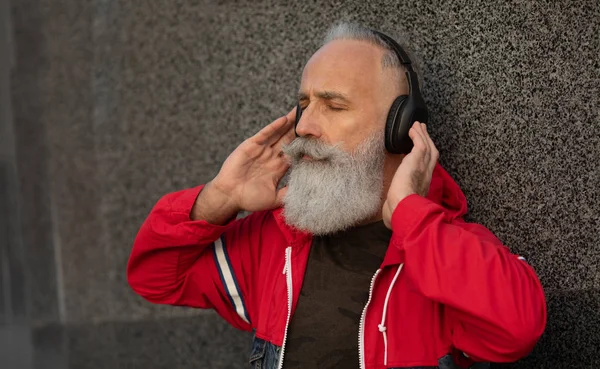 A trendy bearded senior man listening to music outdoor. Fashion mature man.