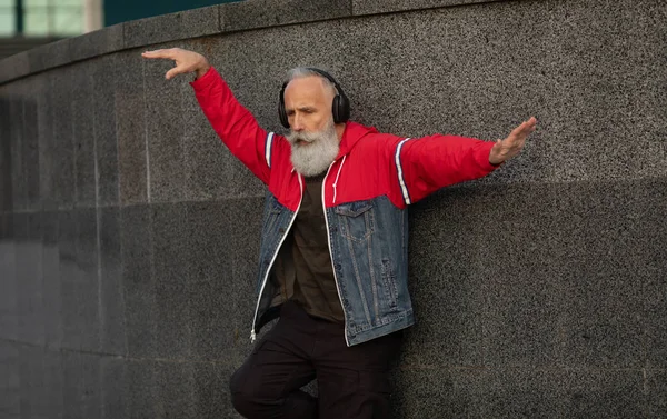 Senior crazy man listening music outdoor. Happy mature male celebrating and dancing outside. Joyful elderly lifestyle concept.