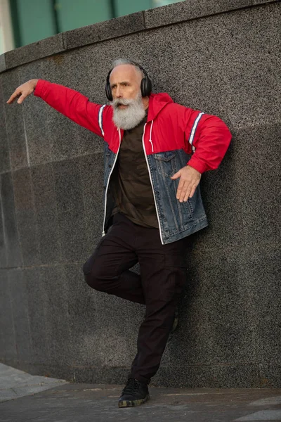 Senior crazy man listening music outdoor. Happy mature male celebrating and dancing outside. Joyful elderly lifestyle concept.