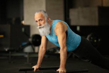 Beyaz sakallı, yakışıklı, kendini beğenmiş, beyaz, yaşlı bir adam göbek ve kollarını güçlendirmek için şınav çekiyor. Tahtada duran çekici, konsantre, emekli bir erkek. Fitness, spor, hobi ve etkinlik.