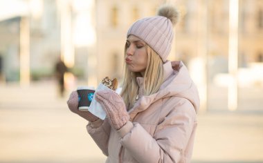Sıcak çay ya da kahveyle sıcak giysiler içinde gülümseyen güzel bir genç kadın. Dışarıda kurabiye yiyen kadın..