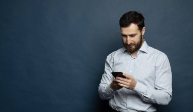 Happy bearded businessman using smartphone over blue background