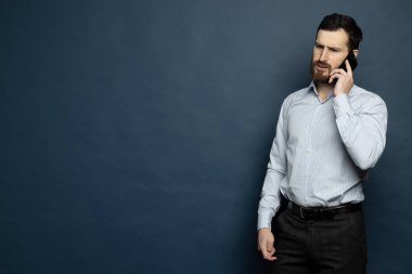 Sakallı bir adam telefonda bağırıyor ve konuşuyor. İzole edilmiş mavi arkaplan.