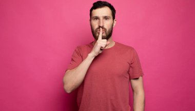 Bearded man placing finger on lips as if to say, shhhhh, be quiet, silence.