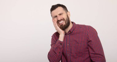 Beyaz arka planda diş ağrısı çeken genç bir adam.