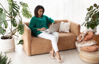 Dizüstü bilgisayarı olan genç siyah kız, parlak oturma odasında oturuyor..