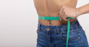 İnce, genç bir kadın, ince belini mezurayla ölçüyor. Yaklaş.