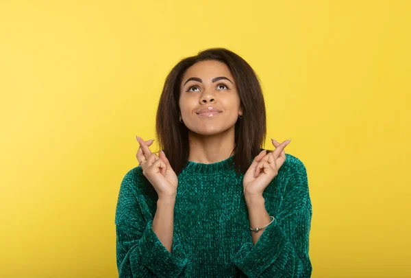Cute black girl crossing fingers wishing, praying for miracle, yellow studio background with copy space.