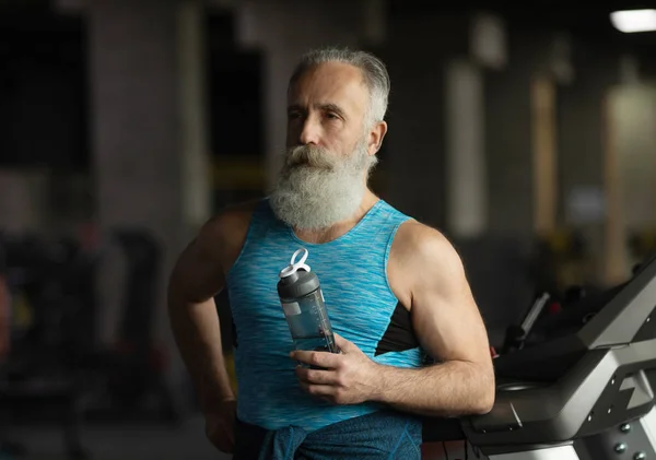 Elderly bearded man in a gym. Resting after exercise