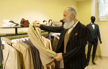 Giyim mağazasında kıyafet alışverişinde takım elbise seçen sakallı kıdemli bir adam..