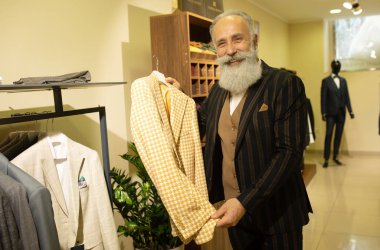 Giyim mağazasında kıyafet alışverişinde takım elbise seçen sakallı kıdemli bir adam..