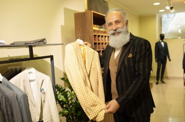 Giyim mağazasında kıyafet alışverişinde takım elbise seçen sakallı kıdemli bir adam..