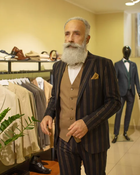 Bearded senior man choosing suit jacket during apparel shopping at clothing store.