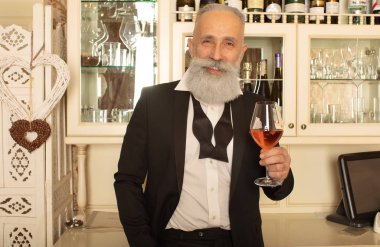 Zarif sakallı beyefendi bir bardak gül şarabıyla kadeh kaldırıp kameraya bakmayı teklif ediyor..