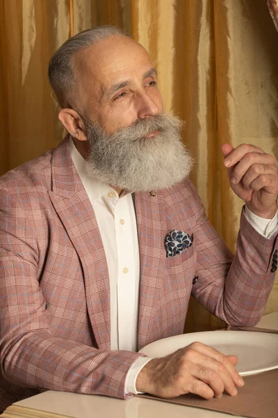 Handsome bearded senior man in a trendy suit sitting in restaurant.