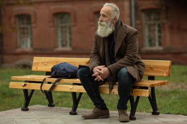 Sakallı yaşlı bir adamın portresi. Parktaki bir bankta oturuyor..