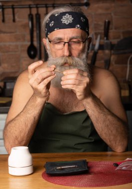 Evde marihuana içen yaşlı sakallı bir adam (esrar, esrar).