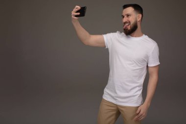 Yakışıklı sakallı adam gri arka planda selfie çekiyor..