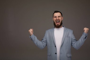 Yakışıklı, sakallı ve takım elbiseli genç bir iş adamı başarı için heyecanlı kollar kaldırarak zaferi kutluyor. Kazanan konsept.