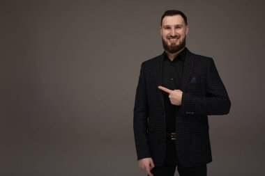 Genç başarılı esmer borsa komisyoncusunun yakın plan portresi gri arka planda, gülümsüyor, takım elbise giyiyor ve parmağıyla bir fotokopi alanını işaret ediyor..