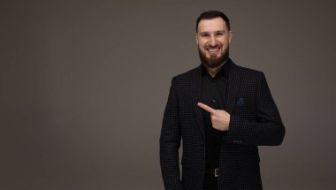 Genç başarılı esmer borsa komisyoncusunun yakın plan portresi gri arka planda, gülümsüyor, takım elbise giyiyor ve parmağıyla bir fotokopi alanını işaret ediyor..