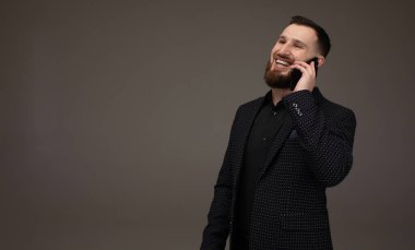 İş ve telefon görüşmesi konsepti. Resmi takım elbiseli adamın telefon konuşması var. Mutlu yüzlü bir iş adamı gri arka planda izole edilmiş. Uzun sakallı adamlar cep telefonu tutarlar..