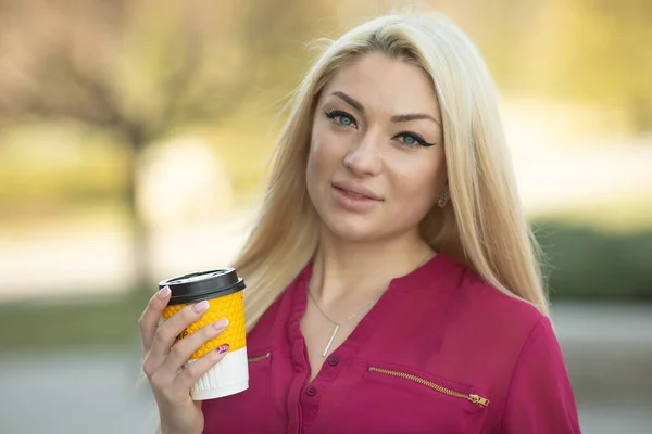 Cheerful fashionable blonde holding coffee outdoors.Young woman drinking coffee on the street of the city.