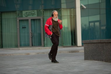 Açık havada müzik dinleyen olgun sakallı bir adamın portresi.