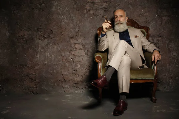 Portrait of an attractive bearded business man with a cigar in a dark room.