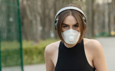 Parkta koşarken tıbbi koruma maskesi takan beyaz kadın portresi. Corona virüsü ya da Covid-19 tüm dünyaya yayılıyor..
