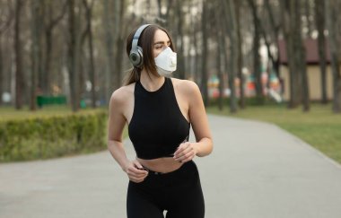 Parkta koşarken tıbbi koruma maskesi takan beyaz kadın portresi. Corona virüsü ya da Covid-19 tüm dünyaya yayılıyor..
