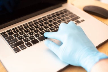 Ofiste ya da evde masa başında dizüstü bilgisayar kullanarak çalışan koruyucu eldivenler giyerek elinizi kapatın. Salgın sırasında Corona virüsü covid-19 'un yayılmasını önlemek.