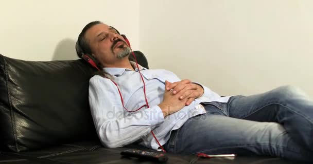 Atractivo morena hombre sentado sofá y escuchar música — Vídeos de Stock