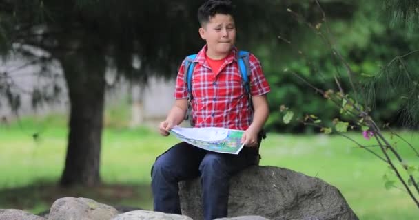 Niño con mapa sentado en piedra en la naturaleza solo — Vídeo de stock