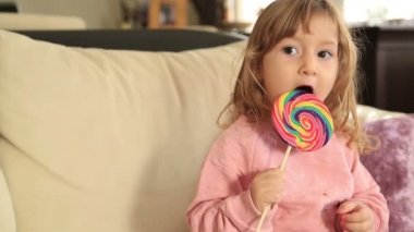 Büyük renkli lolipop tutan uzun, kıvırcık saçlı küçük kız