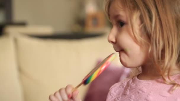 Niña comiendo y lamiendo con lengua grande espiral multicolor caramelo piruleta — Vídeos de Stock