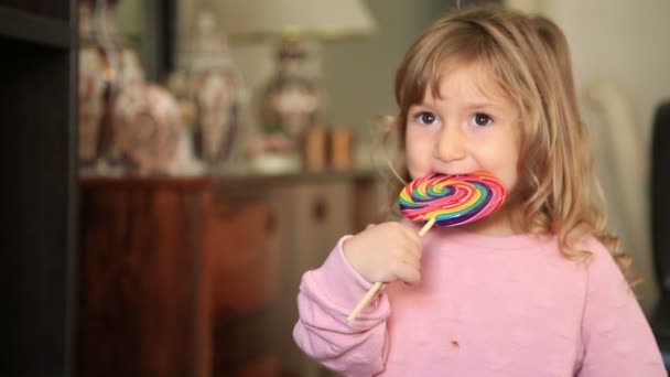 Niña comiendo y lamiendo con lengua grande espiral multicolor caramelo piruleta — Vídeos de Stock