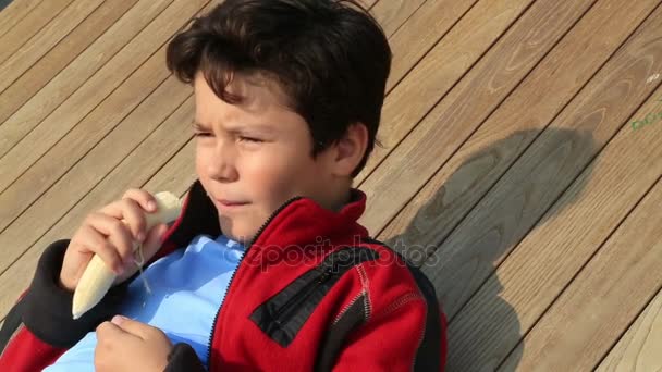 Портрет мальчика, поедающего банан на открытом воздухе — стоковое видео