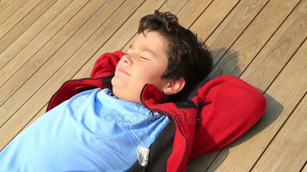 Πορτρέτο του ένα ευτυχισμένο όμορφο νεαρό αγόρι χαλαρώνοντας κάτω από τον ήλιο στο υπαίθριο — Αρχείο Βίντεο