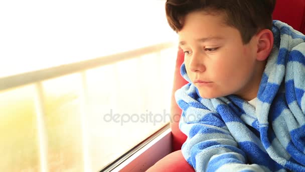 En ung pojke sitter tittar ut genom fönstret — Stockvideo