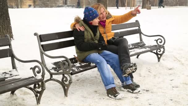 幸せな母と冬の公園で公園のベンチに座っている息子の肖像画 — ストック動画