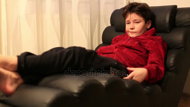 Дитина з пультом дистанційного керування лежить на дивані — стокове відео