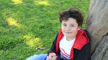Yeşil çimenlerin üzerinde oturan bir gülümseyen çocuk portresi
