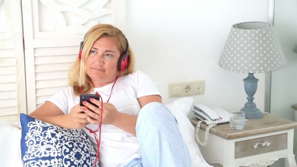 Mujer con auriculares acostada en una cama 4 — Vídeos de Stock