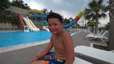 Kameraya bakarak ve gülümseyen aquapark, yüzme havuzunda sevimli genç çocuk portresi