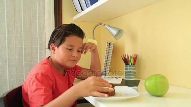 Tiener jongen zijn huiswerk en eten taart — Stockvideo