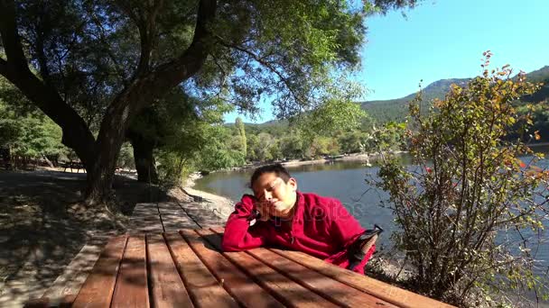 Cute preteen boy sitting on a bench and daydreaming — Stock Video