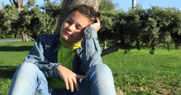 Ung pojke sitter på en gräsmatta och dagdrömmer — Stockvideo