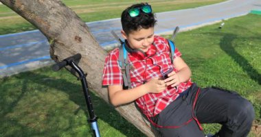 Smartphone kullanarak ve şehir Park'ta rahatlatıcı genç okullu çocuk